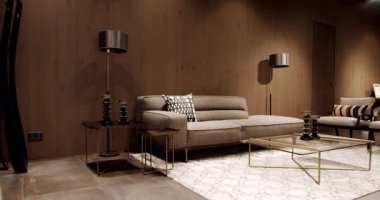 İskandinav iç mimarisi, ahşap duvar, modern gri ve bej kumaş kanepe. Yastıklı tekstil döşeme kanepesi. Modern apartman güzel bej kanepe modern oturma odasında lamba ve halı, masa.
