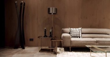 İskandinav iç mimarisi, ahşap duvar, modern gri ve bej kumaş kanepe. Yastıklı tekstil döşeme kanepesi. Modern apartman güzel bej kanepe modern oturma odasında lamba ve halı, masa.