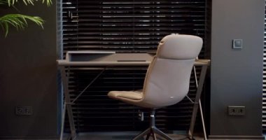 Rahat çalışma odasında minimalist deri koltuklu modern ahşap çalışma masası. Oda palmiyesi dekoru. Minimalist siyah panjurlar. Beauty Interior 'da yatak odası aksesuarı, deri koltuk ve modern masa..