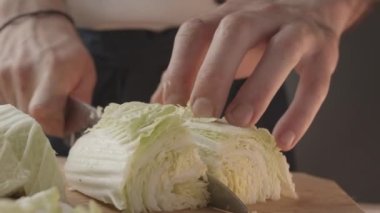 Kesme tahtasında bıçakla ince dilimlenmiş yeşil lahana dilimleri olan genç aşçı önü. Yong Man Cook 'un önü bir parça lahananın ince dilimlerini kesmiş. Sebze. Yakın çekim..