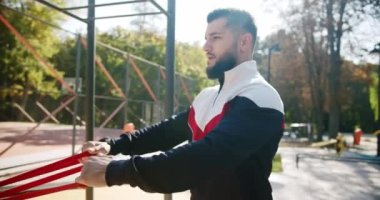 Antrenör erkek düzeltme egzersizleri lastik bant ile yapıyor. Açık hava sporcusu elastik bantla egzersiz yapıyor. Çekici fitness adamı dışarıda egzersiz yapıyor. Spor salonu sağlığı kavramı.