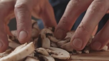 Restoran üniformalı genç aşçı mutfakta çalışır ve elinde mantar tutar, dikkatlice seçer ve yemeği hazırlar. Şampiyon mantarı. vejetaryen yemek detayı.