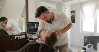 Profesyonel berber, müşteri sakalını ustura ile tıraş eder. Berber dükkanında eski moda bıçakla kesilmiş bir sakal. Yakışıklı adamın sakalını kuaförde traş ettiriyor. Sakalını kes..