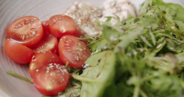 Kiraz domates, roka ve mozzarella, yeşil yapraklar, beyaz arka planda beyaz bir tabakta ıspanak. Vejetaryen yemekleri, organik yiyecekler. Lezzetli salata. Yemek pişirmek. Ağır çekim. Malzemeler. Lezzetli salata. 