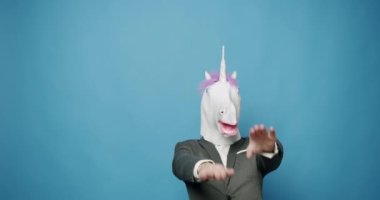 Man with unicorn mask making funny gestures. Business man with Unicorn Mask. Fun and happiness concept. Funny Guy in Gray Suits Dance with Unicorn Mask, he is having fun on isolated Blue Background. 