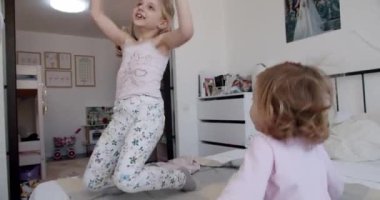 İki küçük kız evde oynuyorlar, sevinçten zıplıyorlar ve güzelce gülümsüyorlar. Evde çocuk aktivitesi. Evde sevimli ve komik kız kardeşler var. Doğal ve mutlu kızlar, mutlu yüzler ve eğlence..