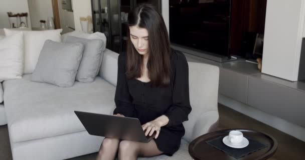ラップトップコンピュータのキーボードでかなり若い白人女性がテキストメッセージを送り 居心地の良いリビングルームのソファに座っています 室内だ ホームレジャー 屋内でリラックス 趣味を書く 自宅でのオンライン仕事 — ストック動画