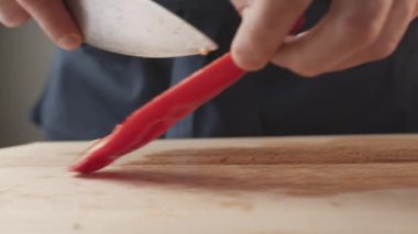 Front view of the young chef cut thin slices of a piece of red pepper with a knife on the cutting board. Front view of a young chef cutting thin slices of a piece of red pepper. Vegetables up close.