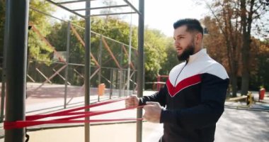 Outdoor Athletic man does exercises with elastic band. Trainer male correcting fit does gym exercises with rubber band . Attractive fitness man does exercising outside. Gym health outside concept.