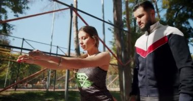 Lastik bantlı kişisel antrenörle açık hava eğitimi. Dışarıda egzersiz yapan genç bir kız. Egzersiz yapan bir kadın. Spor salonu sağlığı konseptin dışında. Antrenör erkek formda kadın jimnastik yapıyor..