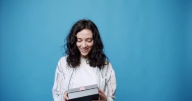 Memnun müşteri, olumlu geri bildirim. E-ticaret web mağazalarından alışveriş, hızlı teslimat konsepti. Genç bir kız güzel paketlenmiş bir kutuda hediye alır, stüdyoda mavi bir arka planda çekilir..