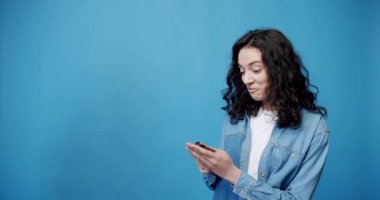 The concept of peoples lifestyle. Looking at the camera, A girl receives a credit card and she is happy, shows the winning gesture. Smiling 20-year-old girl posing on blue background studio. 