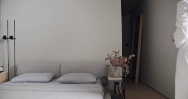 Bedroom in a minimalist apartment in white tones, with modern black lamp. comfortable minimalist interior. elegance home, hotel room, women in robes, contemporary home design. woman enjoys at home.
