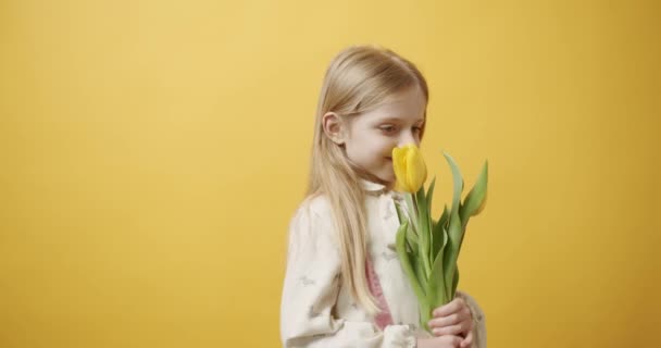 Piękna Dziewczynka Trzyma Ręku Kwiaty Tulipana Uśmiecha Się Odizolowanym Żółtym — Wideo stockowe