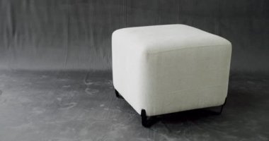 Modern white Ottoman on gray isolated background. Cosy seat with minimalist pouf. Decor for Luxury apartment. Comfortable white fabric pouf. Elegant Square puff.