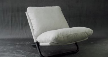 Truck shot of interior detail design of modern white chair at home. White fabric minimalist chair on modern isolated gray background. Comfortable cosy Chair. Home sitting on modern relaxing armchair.