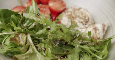 Kiraz domates, roka ve mozzarella, yeşil yapraklar, beyaz arka planda beyaz bir tabakta ıspanak. Vejetaryen yemekleri, organik yiyecekler. Lezzetli salata. Yemek pişirmek. Ağır çekim. Malzemeler. Lezzetli salata. 