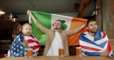 Men with the flag of the international country drinking beer and watching sport game. Soccer fans celebrating victory of team in sports bar. Happy supporters cheering and exulting after winning