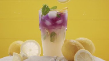 Limon parçaları ferahlatıcı yaz limonata kokteylinin içine düşer yaz ferahlatıcı kokteyl, sarı arka planda deniz kumu ve tropikal yapraklarla çekilen stüdyo çekimi. Citrus Kireç Kokteyli. Tonik..