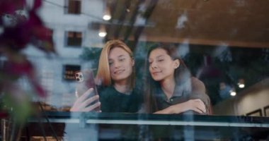 Two girls rest and serve coffee and tea outside at morning work day, converse and smile outside near a terrace, lifestyle coffee time. The girls take pictures with their phones. Self pictures