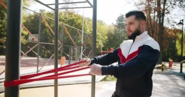 Attractive fitness man does exercising outside. Trainer male correcting fit does gym exercises with rubber band . Outdoor Athletic man does exercises with elastic band. Gym health outside concept.