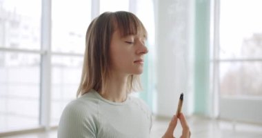 Woman meditating with Palo Santo, holy wood, relaxation zen practice in studio, herbal healing, yoga or aura cleaning. Bursera Graveolens. Essential incense for esoteric rituals.