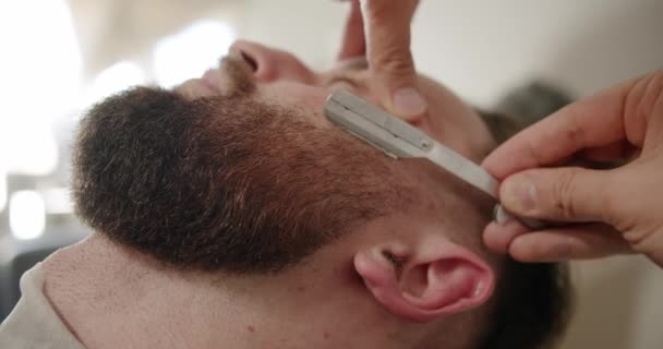 专业理发师用直剃须刀刮胡子 理发店用老式刀片剪胡子 特写帅哥在理发店刮胡子 刮胡子 — 图库视频影像