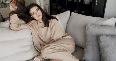 Calm young woman having healthy daytime, relaxing on couch with eyes closed and hands behind head, peaceful girl sleeping breathing fresh air resting leaning on comfortable sofa at modern home.