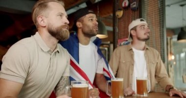 Fans watching football in a bar with friends. Loyal football fans supporting their team. Men with the flag of the national country of Great Britain drinking beer and watching sport game.