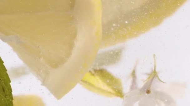 マクロクローズアップライムスライスと冷たい弾力のあるさわやかな飲み物のガラス 透明な水に黄色のレモン柑橘類商業ジュースのための新鮮な果物 レモンフルーツ夏ドリンクをスライスします ソーダカクテル — ストック動画