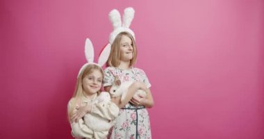 Tavşan kulaklı şirin kızlar izole edilmiş pembe arka planda tavşanla oynuyorlar. Şirin tüylü tavşan, sevimli hayvan konsepti. Mutlu Paskalyalar. Bahar tatili. Kutlama etkinliği.