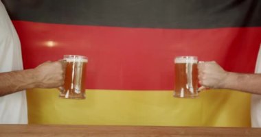 Genç Halkların elleri, Almanya 'nın arka planına karşı bira dolu bardaklar gibi çarpışıyor. Futbol fanatikleri takımın zaferini spor barında kutluyorlar. Word Cup destekçileri. Bardaki arkadaşlar eğleniyorlar.