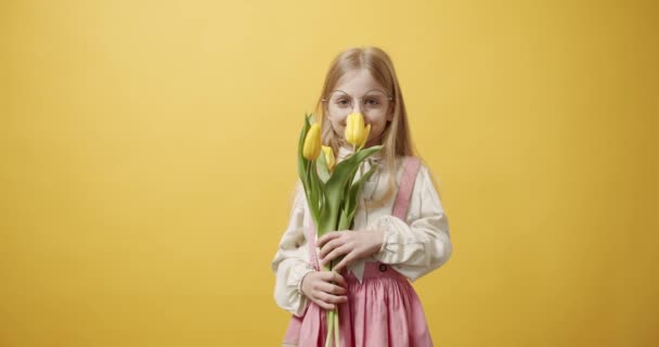美しい少女は手にチューリップの花を持っている 彼女は孤立した黄色の背景に笑顔 春の花の花束を持つ小さな子供の肖像画 テキストのためのスペース 春のコンセプト — ストック動画