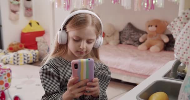 소녀는 아이들 방에서 헤드폰을 스마트폰을 사용하며 비디오나 사진을 네트워크에서 즐기고 — 비디오