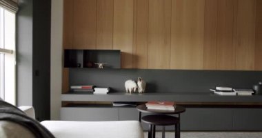 Minimalist İç İşleri. Samimi Modern Mobilya Tasarımı. Ahşap duvarlı ve gri mobilyalı modern Minimalist oturma odası. Köşedeki kanepe ve kitaplığı olan modern ev iç mimarisi.