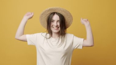 Casul Woman Smiling and she sit happy, jumps up and joy on Yellow Background in Slow Motion. emotion winner. Excitement and a fulfilled wish concept. Lucky Girl happy with hat and white T-shirt.