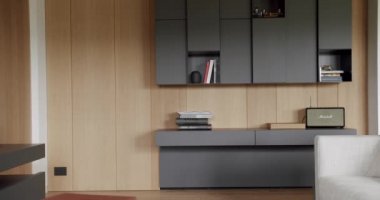 Ahşap duvarlı ve gri mobilyalı minimalist oturma odası. Köşedeki kanepe ve kitaplığı olan lüks bir ev. Minimalist İç İşleri. Rafları ve kitabı olan rahat Modern Mobilya Tasarımı.