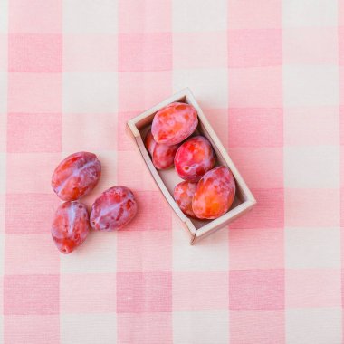 Tekstil arka planında taze pembe erikler. Kareli masa örtüsünün üzerinde tahta bir kabın içinde olgun meyveler.