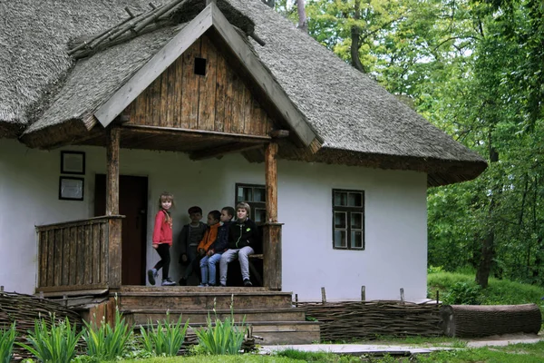 Ukrainian children sitting together on porch of ukrainian authentic traditional country house hata cottage in village outdoor in May