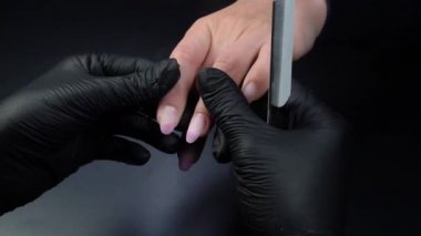 Siyah eldivenli bir kadının güzellik salonunda manikür üzerinde çalışmasını yakından izleyeceğiz.