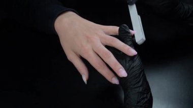 Siyah eldivenli bir kadının güzellik salonunda manikür üzerinde çalışmasını yakından izleyeceğiz.