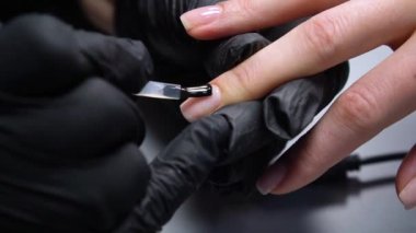 Siyah eldivenli bir kadının güzellik salonunda manikür üzerinde çalışmasını yakından izleyeceğiz.