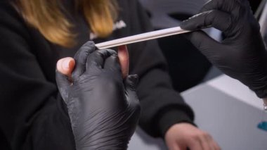 Siyah eldivenli bir kadının güzellik salonunda manikür üzerinde çalışmasını yakından izleyeceğiz.