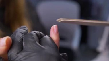 Siyah eldivenli bir kadının güzellik salonunda manikür üzerinde çalışmasını yakından izleyeceğiz.