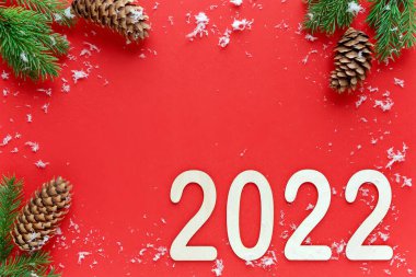 Kırmızı Noel arka planının üst görüntüsü, köşelerde ladin dalları ve köknar konileri, beyaz kar taneleri, yeni yıl 2022 'nin sağ alt köşesinde, kopyalama alanı.