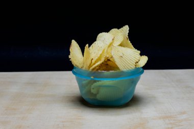 Masadaki hafif mısır gevreğinde tuzlu patates cipsleri, siyah arka planda izole edilmiş waffle cipsleri.