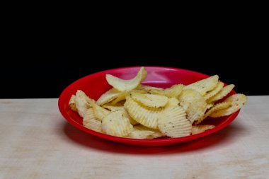 Tahta Masa 'da kırmızı tabakta tuzlu patates gofretleri, bir yığın gofret, kopyalama alanı, cips yığını, yan görüş, siyah arka planda izole edilmiş.