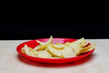 Tahta Masa 'da kırmızı tabakta tuzlu patates gofretleri, bir yığın gofret, kopyalama alanı, cips yığını, yan görüş, siyah arka planda izole edilmiş.