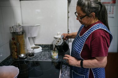 Yaşlı kadın cam bardaktan kendine kahve dolduruyor.