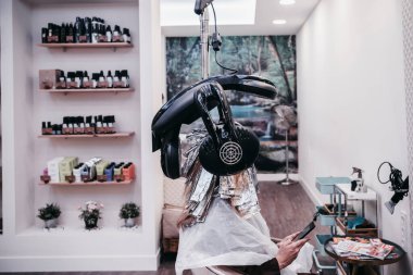 Güzellik salonunda cep telefonuna bakan gülümseyen kadın.